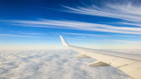 The plain white wing of an airliner at cruising altitude above a flat cloud deck, with long parallel bands of high cirrus streaked across a deep blue autumn sky.